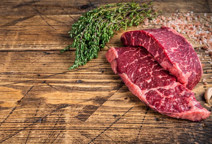 Raw denver or top blade meat steak on a butchery table with herbs. wooden background. Top view. Copy space.