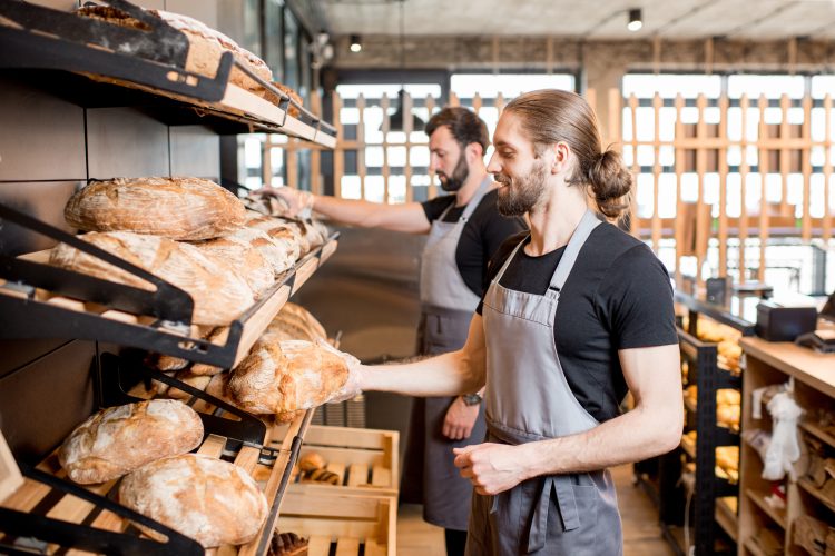 Handsome sellers putting bread loafs on the shelves of the bakery shop